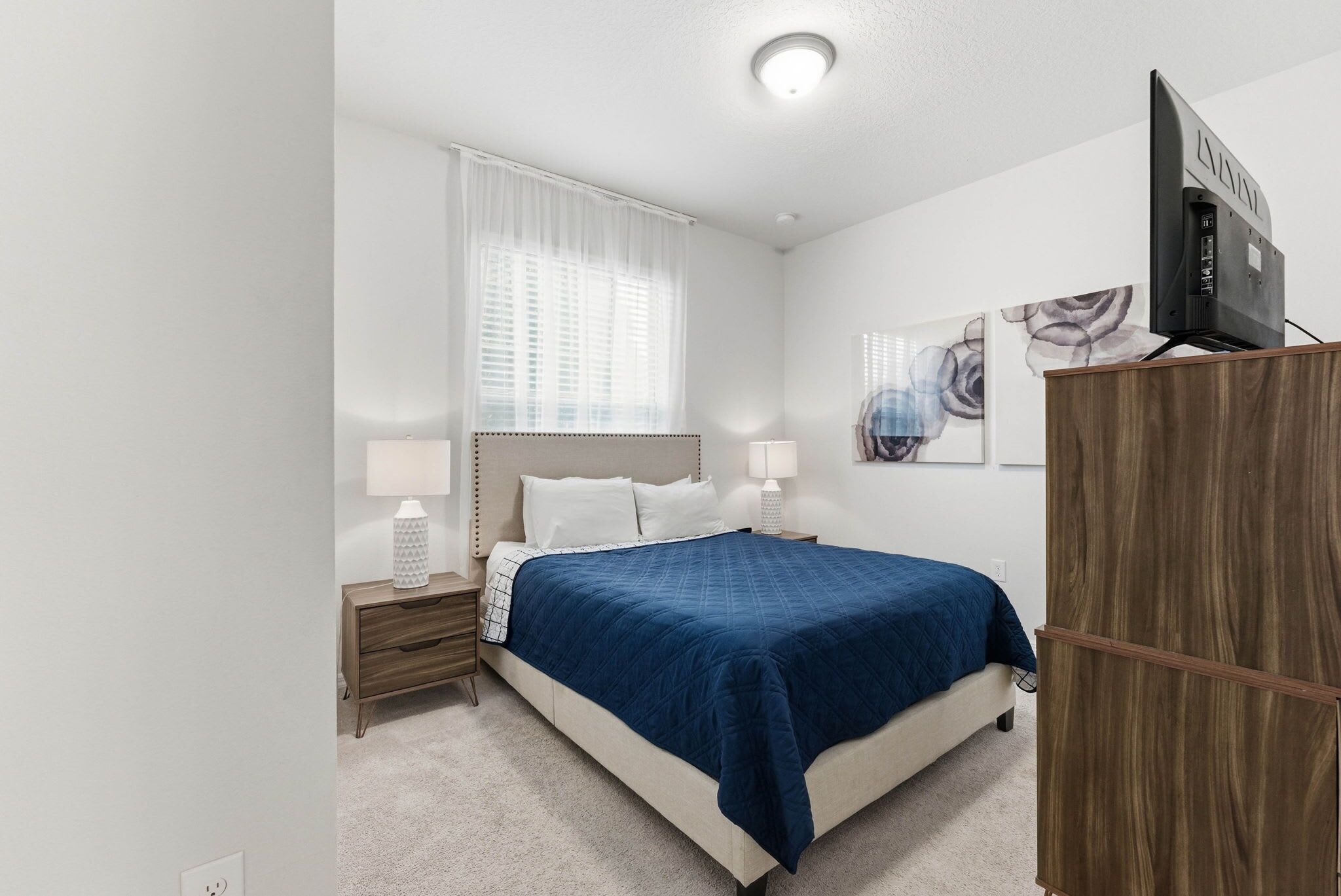 Een slaapkamer met een bed, nachtkastjes, een televisie en kunstwerken aan de muur.