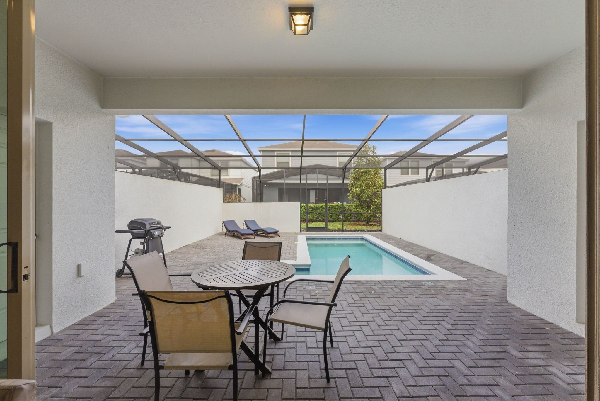 A patio with a pool, lounge chairs, and a grill.
