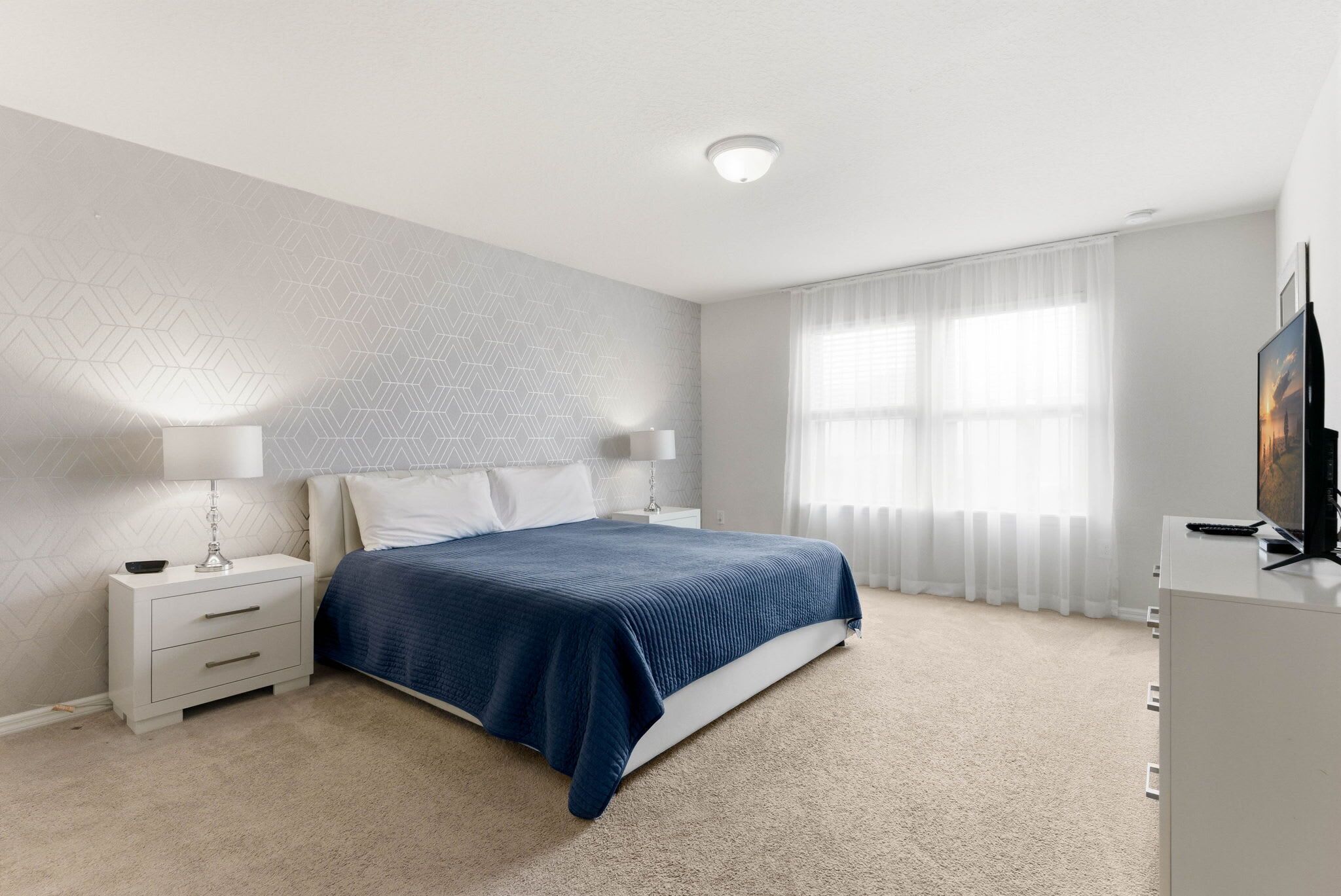 A bedroom with a bed, nightstand, lamp, and a TV.