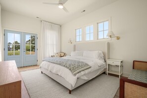 A bedroom with a bed, bedside tables, a nightstand, a desk, a chair, and a view through a door.