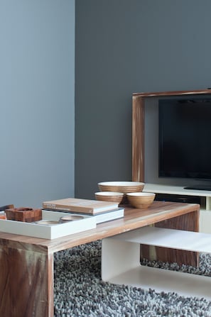Ein modernes Wohnzimmer mit Flachbildfernseher, Couchtisch aus Holz und Bücherregal.