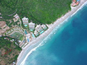 Luftaufnahme eines Küstenresorts mit mehreren Gebäuden, einem Strand und einer großen Wasserfläche.