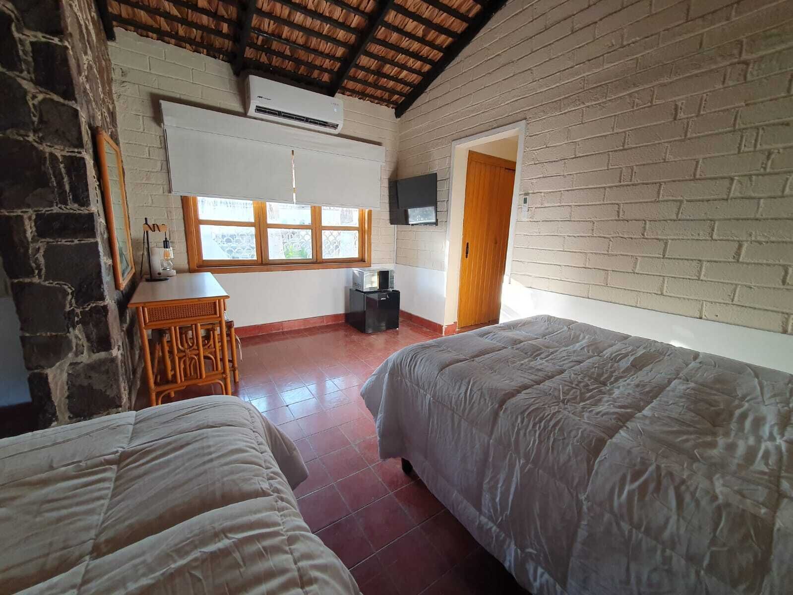 Una stanza con due letti, una televisione appesa al muro, una finestra e una porta.