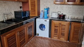 Uma cozinha compacta com máquina de lavar, micro-ondas e panela elétrica.