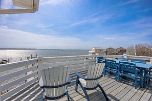 A deck with chairs and tables overlooking a body of water, with buildings in the background. - Bay Dreams Soundfront Escape w/ Beach Parking & Sunsets (Kill Devil Hills)