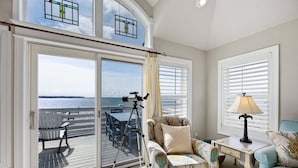 Ein Zimmer mit einer großen Glasschiebetür, die auf einen Balkon führt, einem Sessel, einem Tisch und einer Lampe.