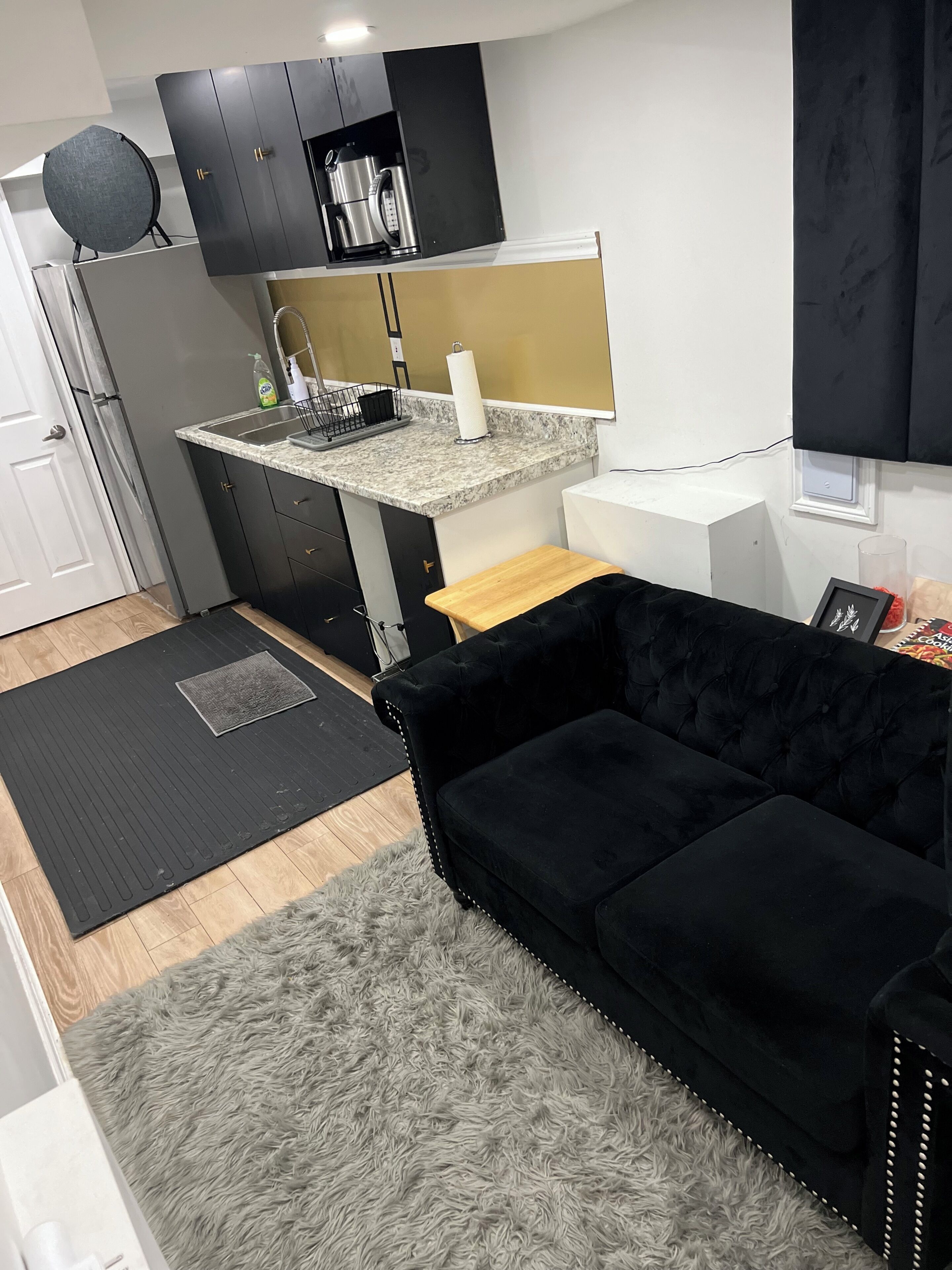A compact kitchen with a black sofa, a small rug, and a wooden coffee table.