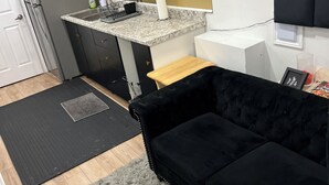 Une cuisine de taille réduite avec un canapé noir, un petit tapis et une table basse en bois.
