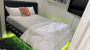 Une chambre avec deux lits, une tête de lit noire, un tapis vert et un téléviseur fixé au mur.
