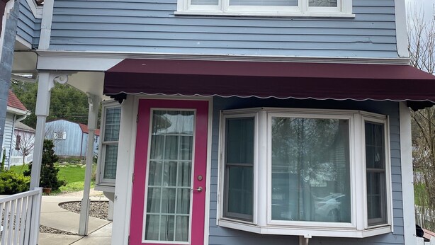A two-story house with a covered porch, a pink door, and a large window.