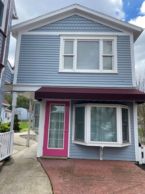A two-story house with a covered porch, a pink door, and a large window.
