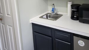 A kitchen with white cabinets, a stainless steel sink, a coffee maker, and a refrigerator.