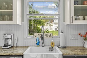 Una cocina con ventana, cafetera, lavamanos y un letrero que dice 'BEACH HOUSE'.