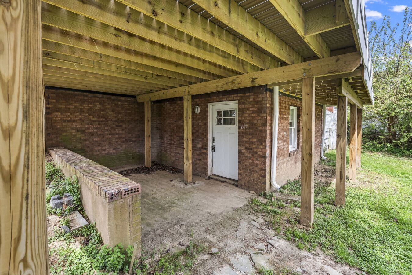 A covered outdoor area with a brick wall, a door, and a wooden structure.