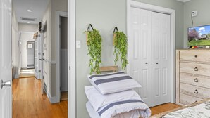 Une chambre à coucher comprenant un lit, une commode, un téléviseur et deux plantes suspendues.