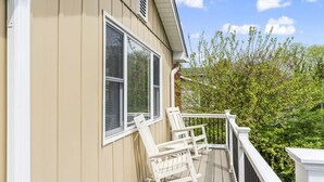 Une terrasse en bois avec des fauteuils à bascule blancs et une balustrade blanche.