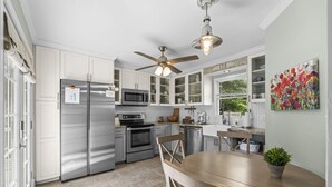 Une cuisine moderne équipée d’appareils électroménagers en acier inoxydable, un coin repas avec une table en bois et un ventilateur de plafond.