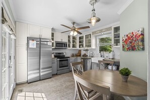Una cocina moderna con electrodomésticos de acero inoxidable, un comedor con mesa de madera y un ventilador de techo.