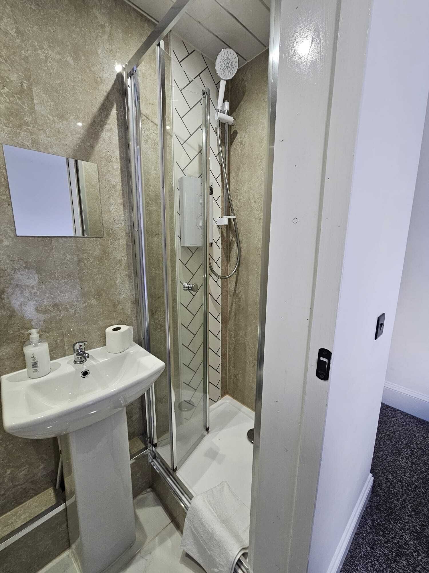 A bathroom with a glass-enclosed shower, a sink with a mirror, and a towel rack.