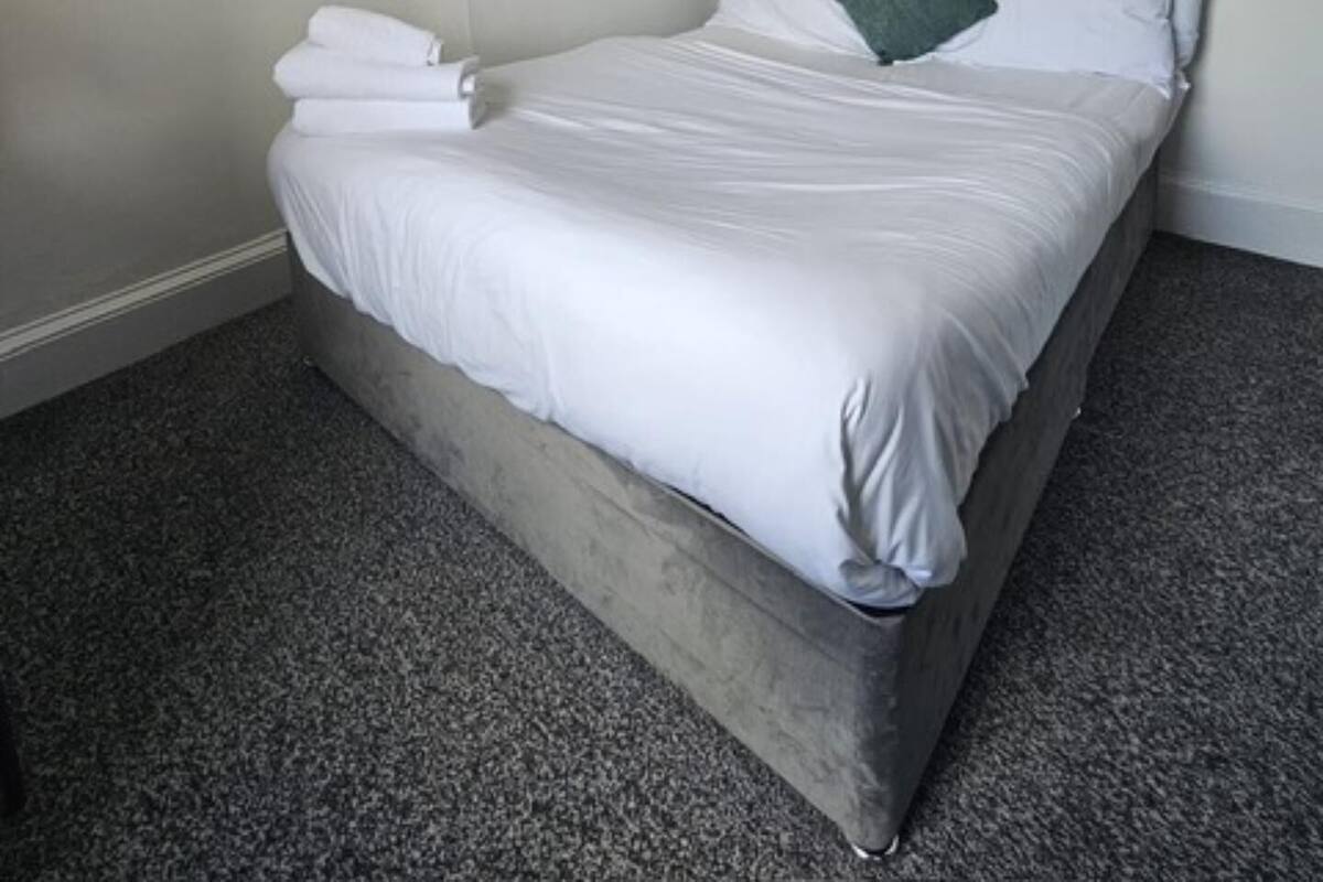 A single bed with white linens, a dark grey headboard, and a green pillow.