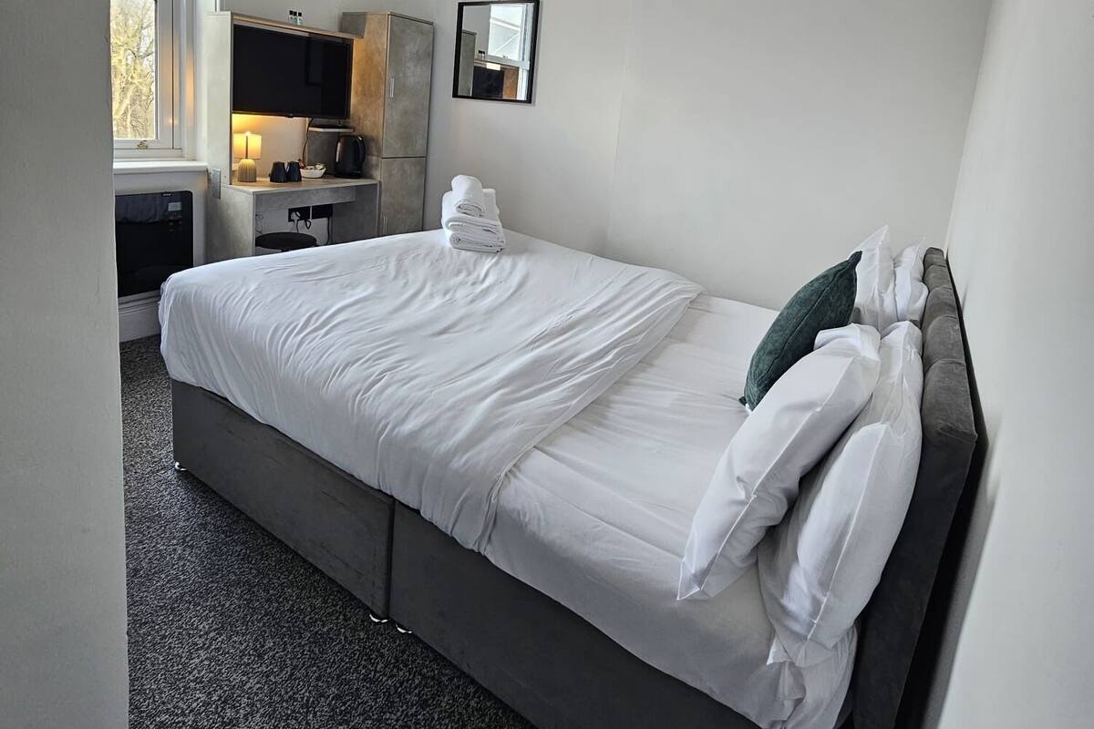 A bedroom with a bed, a desk, a chair, a wardrobe, and a mirror.