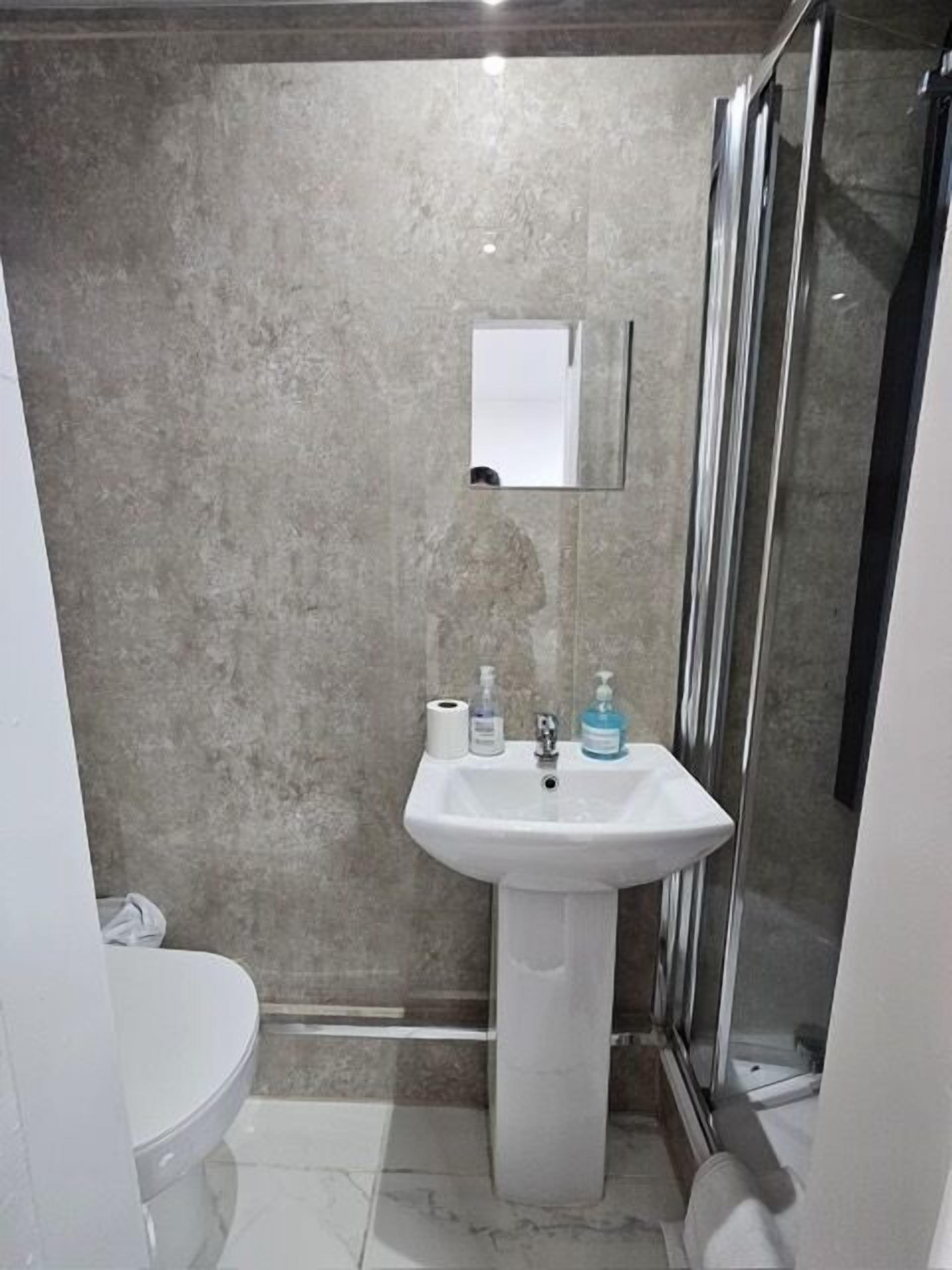 Un baño con lavamanos pedestal, inodoro y cabina de ducha de cristal.