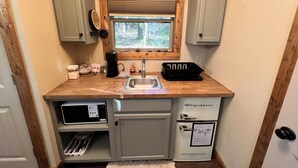A compact kitchen with a sink, a microwave, a refrigerator, and a window with a view of the outdoors. - Cozy Ozark Cottage Near Spring River & Mammoth Spring (Mammoth Spring)