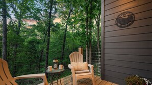 A wooden deck with a chair and table, surrounded by a forest. - Cozy Ozark Cottage Near Spring River & Mammoth Spring (Mammoth Spring)