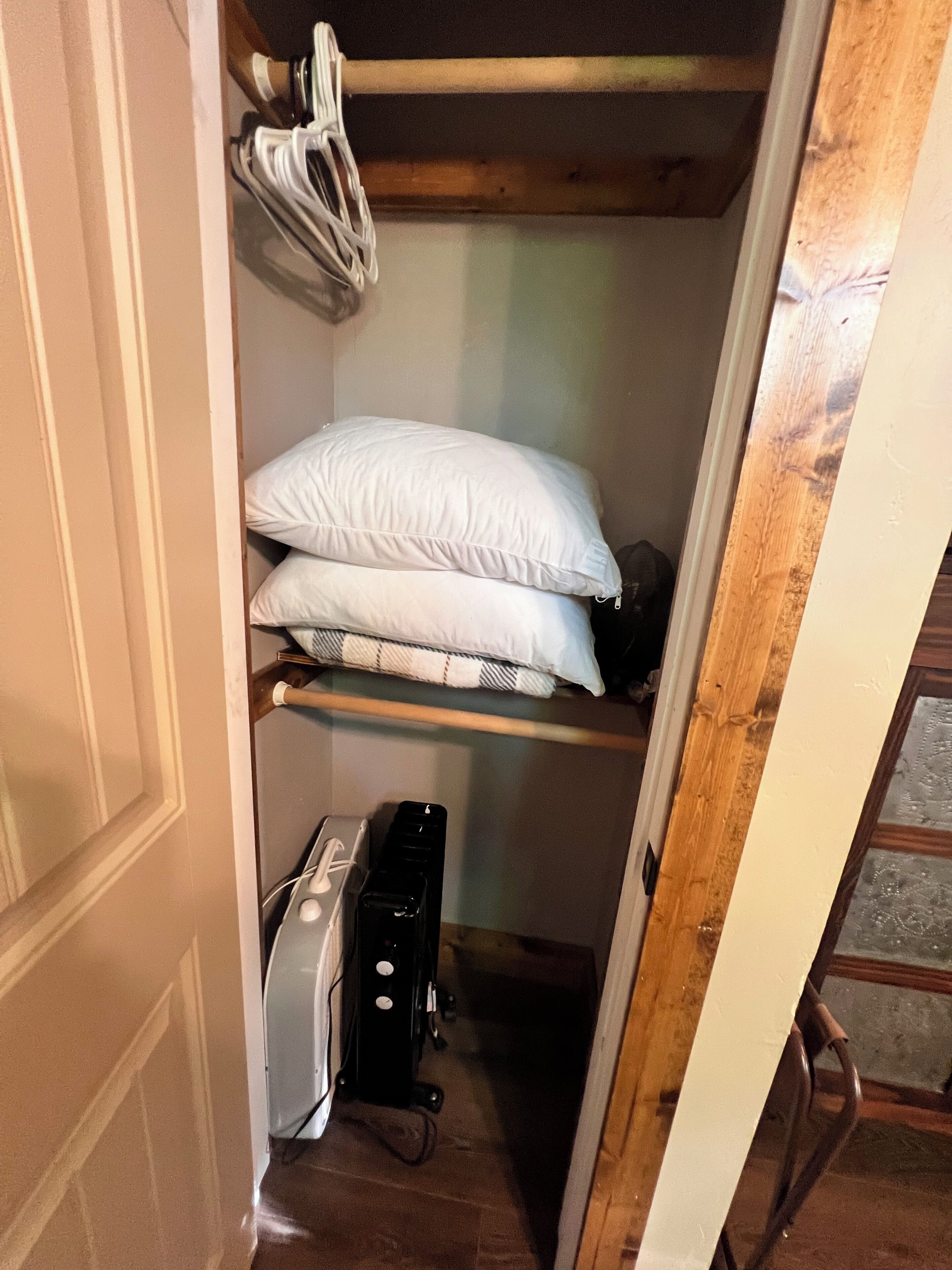 A small, narrow closet with a wooden ladder, a shelf with white pillows, and a black appliance on the floor.