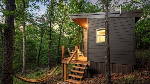A cabin with a wooden staircase leading to a deck, surrounded by trees. - Cozy Ozark Cottage Near Spring River & Mammoth Spring (Mammoth Spring)
