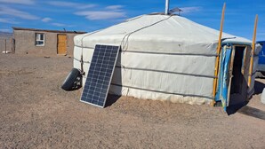 Une yourte dotée d’un panneau solaire, un petit bâtiment attenant et un ciel dégagé.
