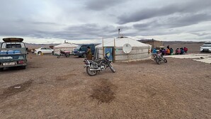 Des yourtes, une moto et une voiture, dans un paysage aride et dégagé.