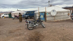 Une yourte avec une antenne parabolique, une moto et une voiture blanche garée à proximité.