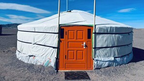 Une yourte dotée d’une porte centrale et de deux poteaux, installée dans un paysage désolé.