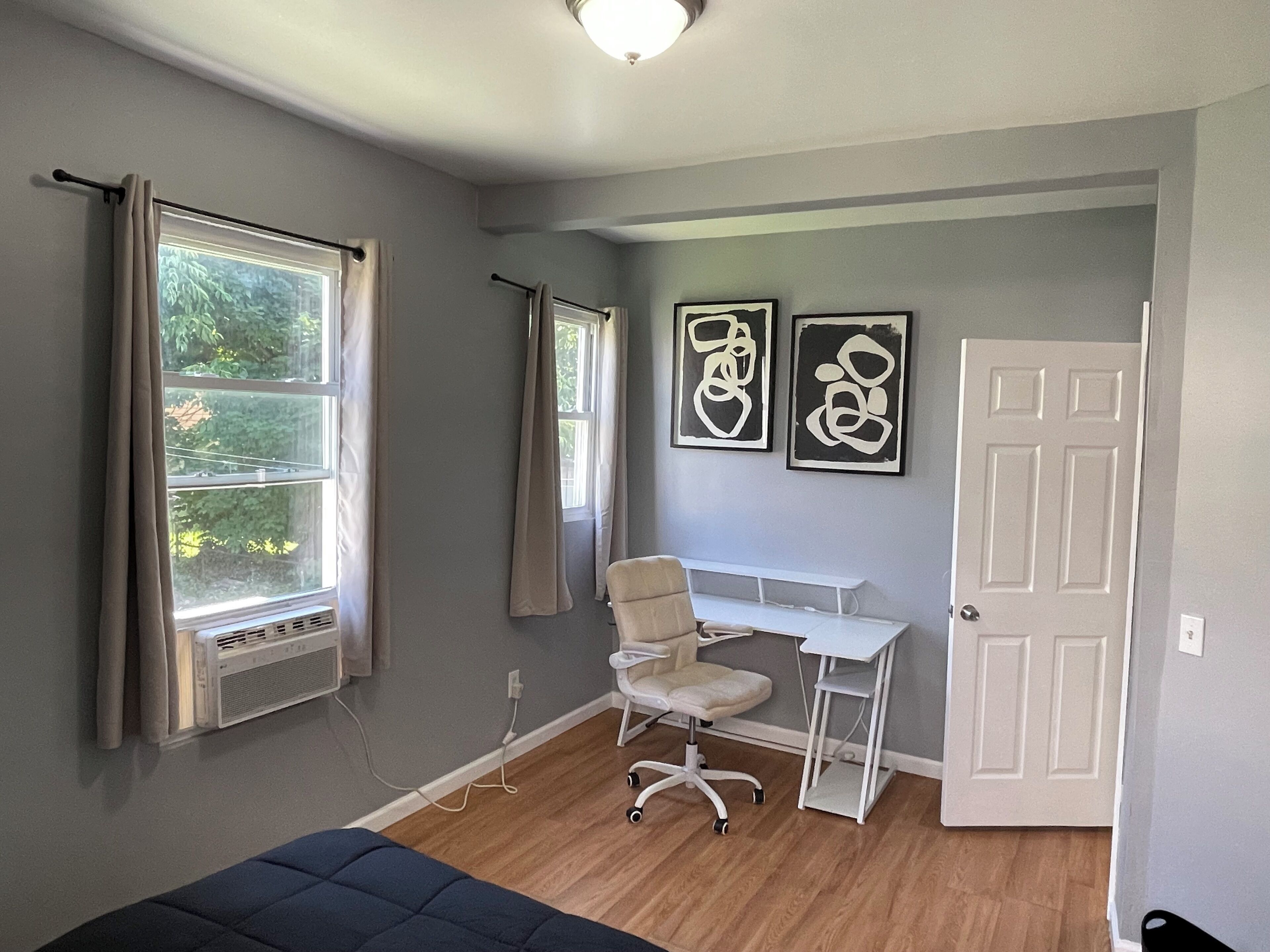 Una habitación con cama, escritorio, silla, radiador y dos ventanas con cortinas.