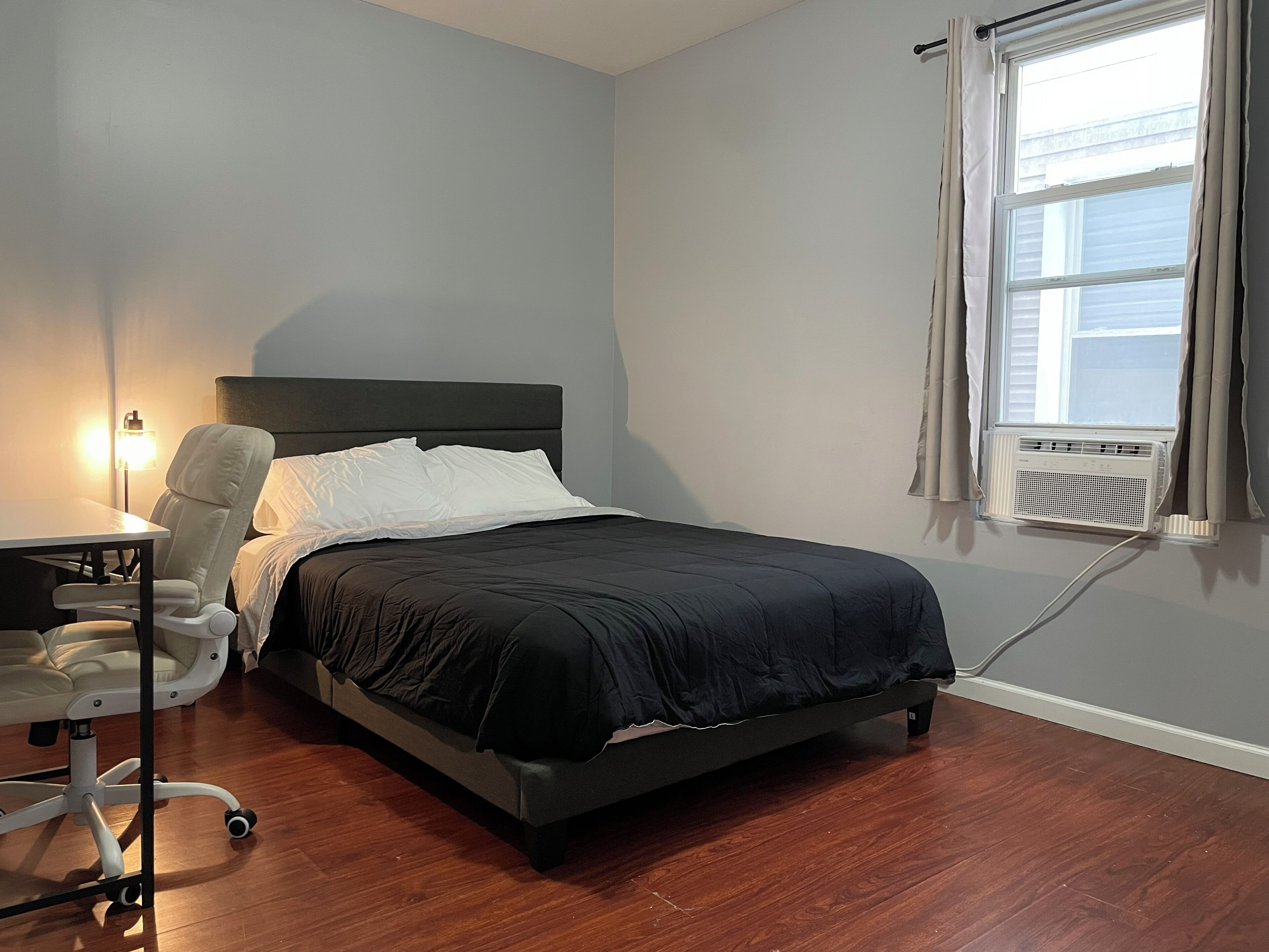 A bedroom with a bed, a desk, a chair, and a window with curtains.