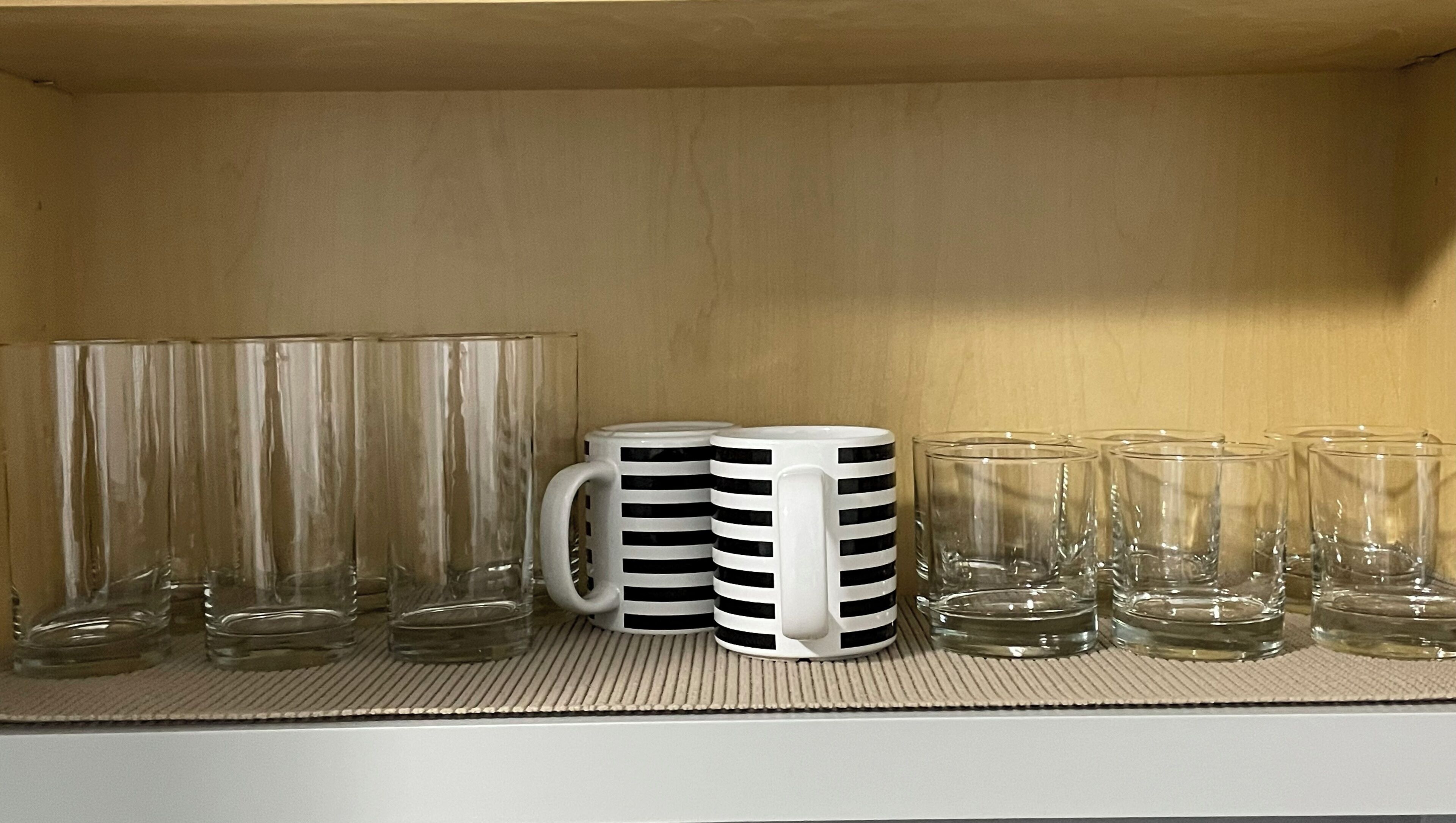 Une étagère contenant divers objets en verre, notamment des verres transparents et une tasse blanche à rayures noires.