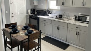 Een kleine keuken met een eettafel, stoelen, een kookplaat, een spoelbak en kastjes.