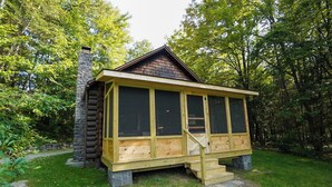 Eine Blockhütte mit Schornstein, großen Fenstern und einer Holztreppe, die zum Eingang führt.