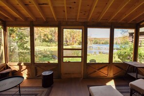 A cabin interior with large windows, wooden beams, and a view of a lake and forest. - Relaxing Lakeside Resort-Cabin 6 (Olmstedville)