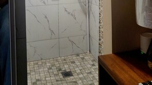 Une salle de bain avec une douche, des carreaux de marbre, une étagère blanche, des toilettes et un comptoir en bois.