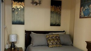 Une chambre à coucher comprenant un lit, une table de chevet, une lampe, un ventilateur de plafond et des œuvres d’art accrochées aux murs.