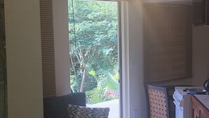 Un salon avec un canapé, une petite table, un ventilateur de plafond et une vue sur la verdure à l’extérieur.