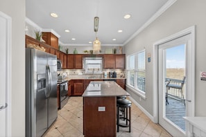 A kitchen with a central island, stainless steel appliances, wooden cabinets, and a view through the door.