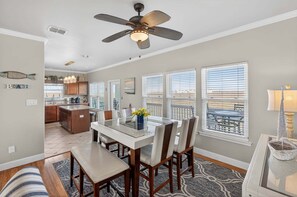 A dining area with a glass table, wooden chairs, and a ceiling fan.