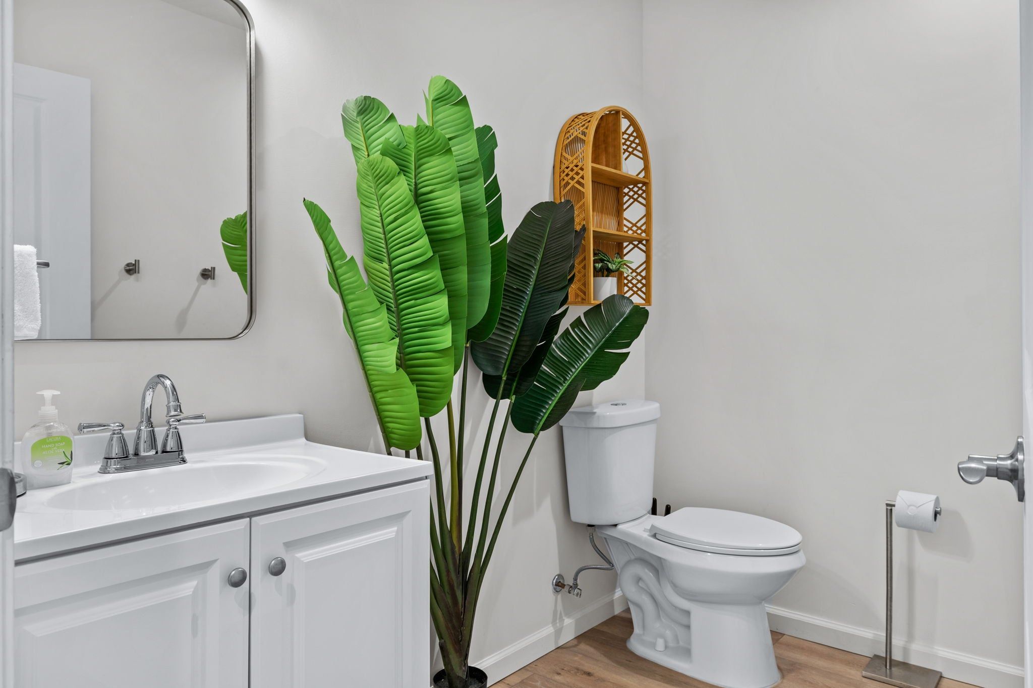A bathroom with a white sink, mirror, toilet, and a large potted plant.