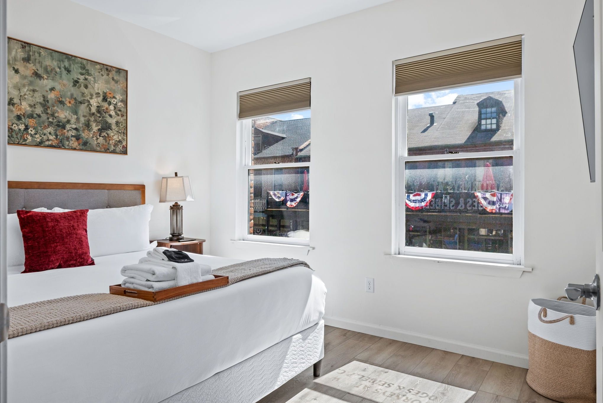 Bedroom with a made bed, bedside lamps, and two windows.