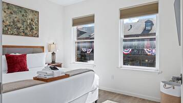 Bedroom with a made bed, bedside lamps, and two windows.