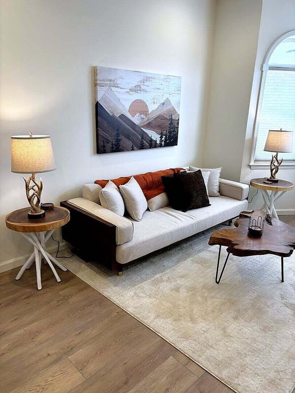 A living room with a sofa, two side tables, a rug, and a wall-mounted painting.