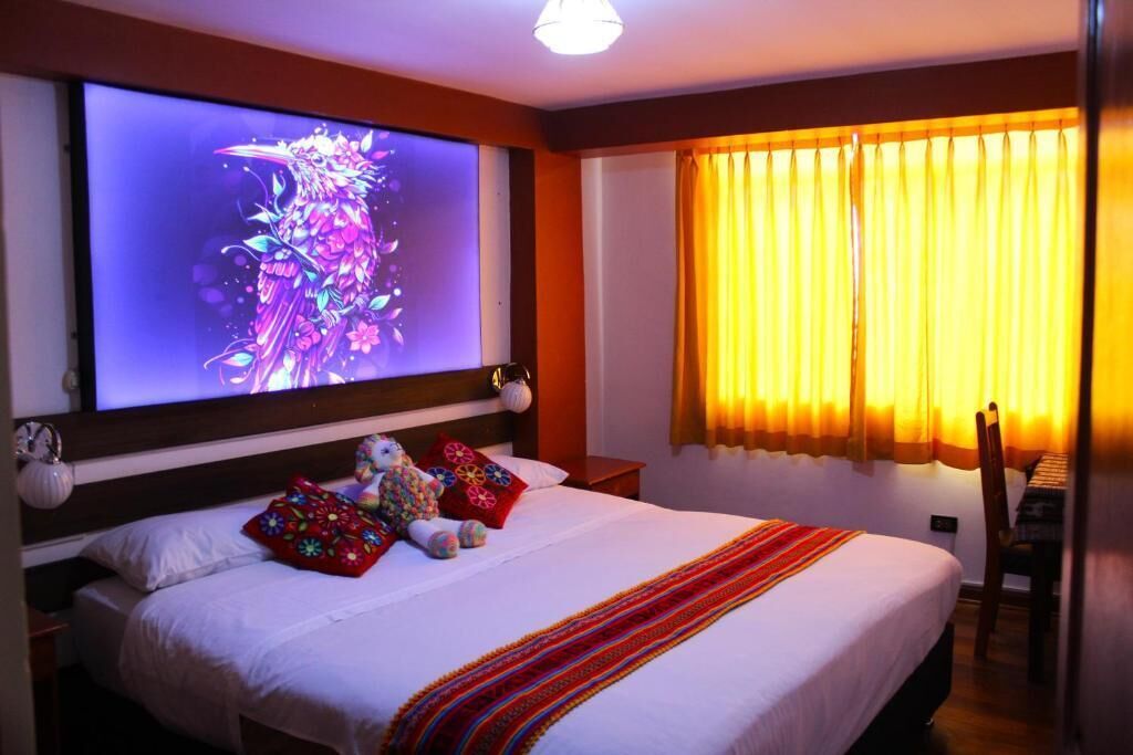 Habitación de hotel con cama, una pantalla de televisión grande, una ventana con cortinas y una silla.